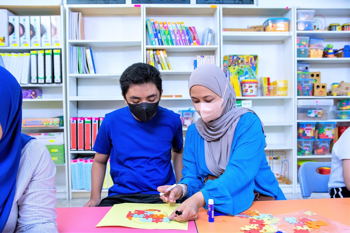 A mother works on a puzzle with her autistic son in a classroom.