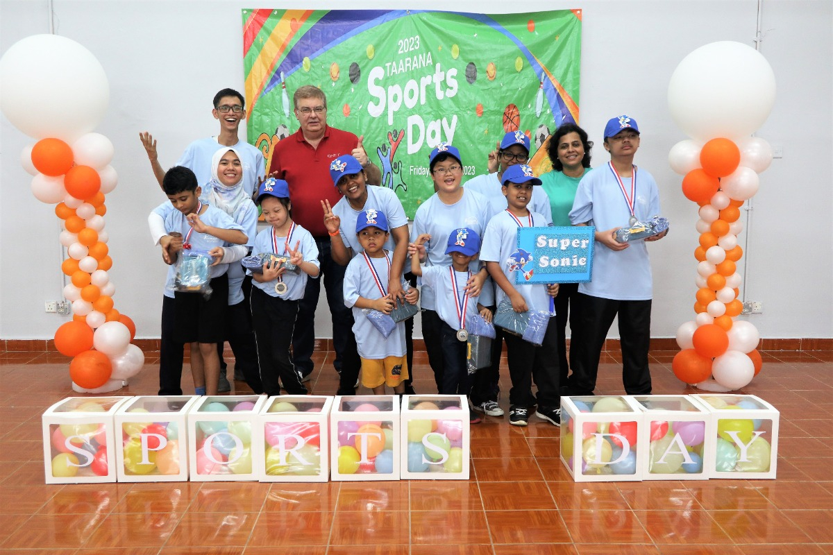 A group of adults and children on stage during a school sports day.