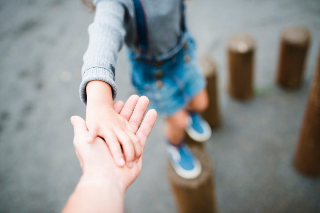 A child's hand being gently guided by a caring adult's hand.