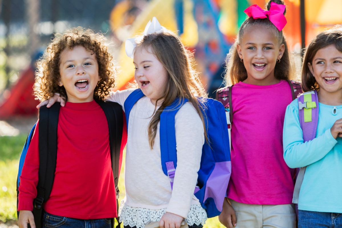 A smiling Down syndrome child with a group of typical children in a playground.