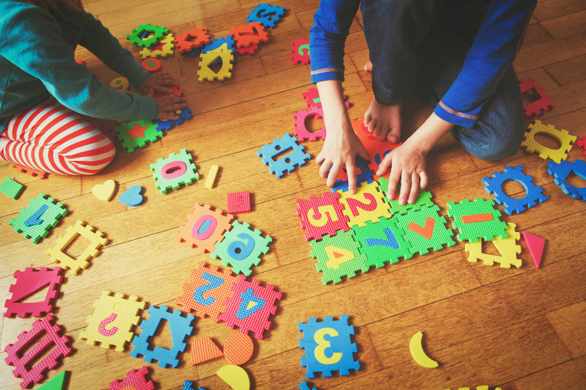 Children sit on a wooden floor playing with a puzzle.