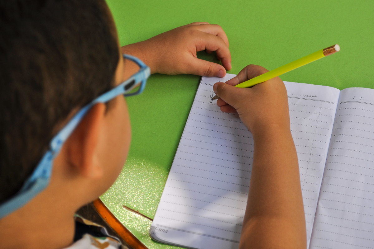 Close-up shot of a child writing on a notebook using a pencil.