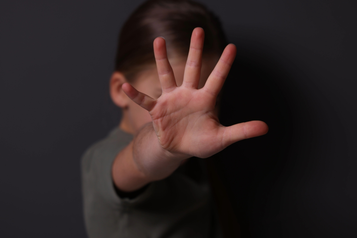 A girl makes a stop gesture near a gray wall.