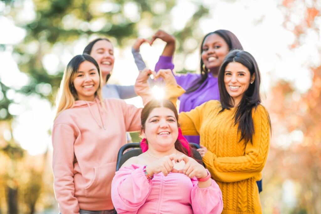 Group of smiling girls, including one in a wheelchair, forming hearts to support siblings of children with special needs.