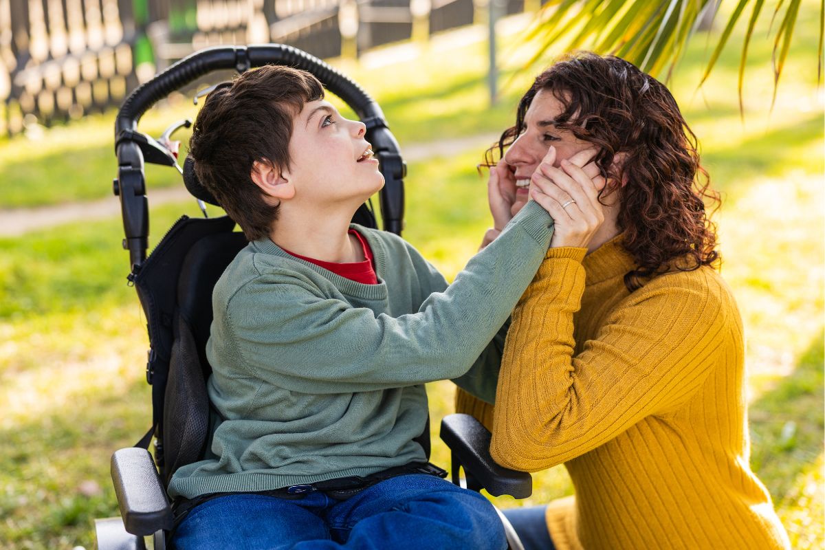 A child in a wheelchair smiling and touching a woman's face, showing connection with siblings of children with special needs.